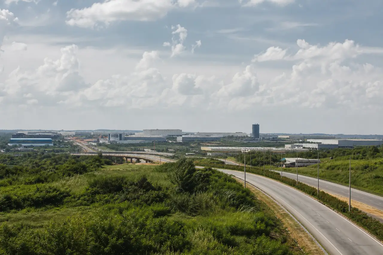 Distant industrial corridor and road infrastructure beyond a green verge